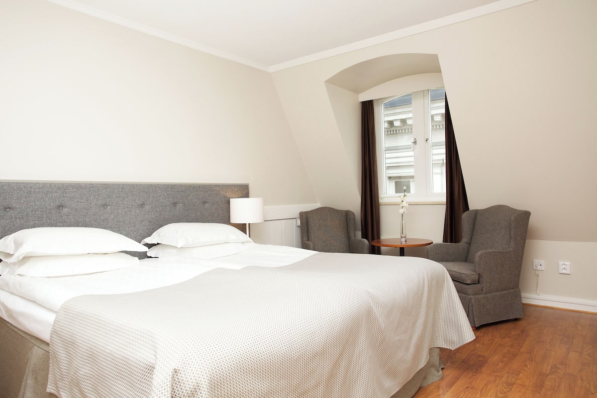 A hotel room with a bed, two armchairs, a small table, and a window with curtains.