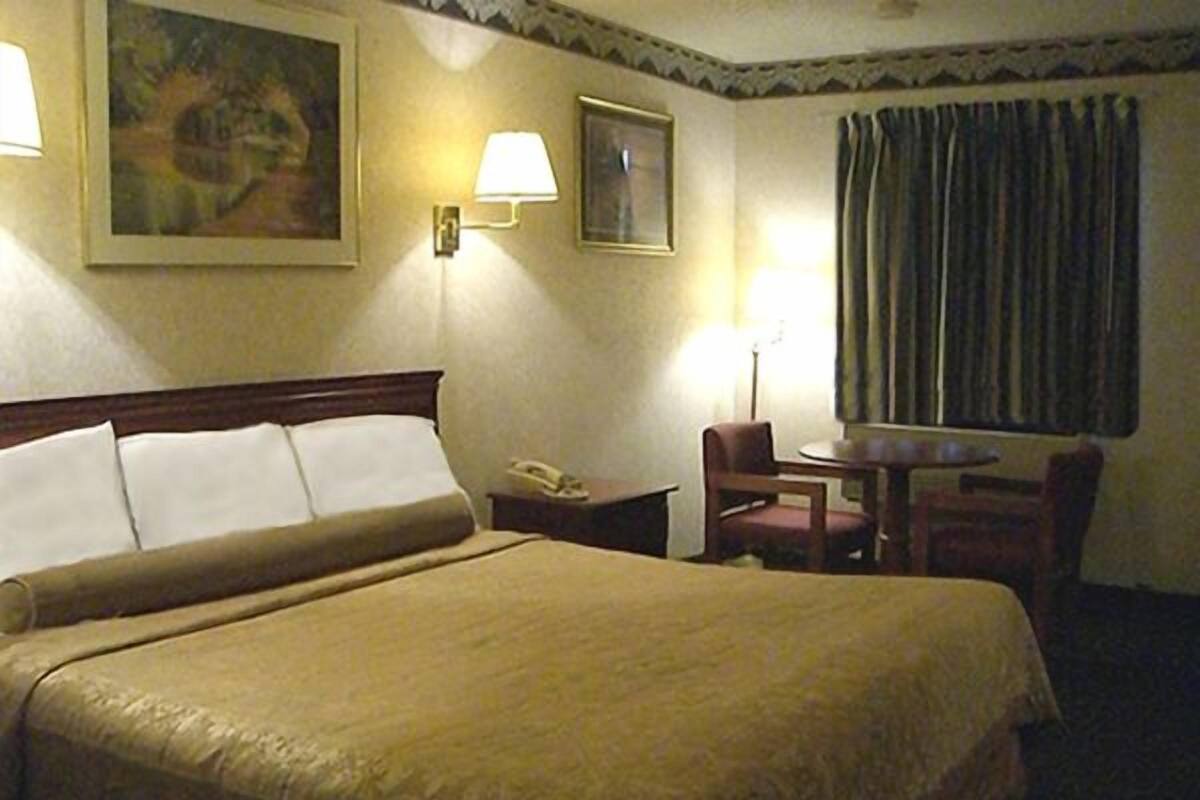 A hotel room with a large bed, a desk with a telephone, a chair, and a window with curtains.
