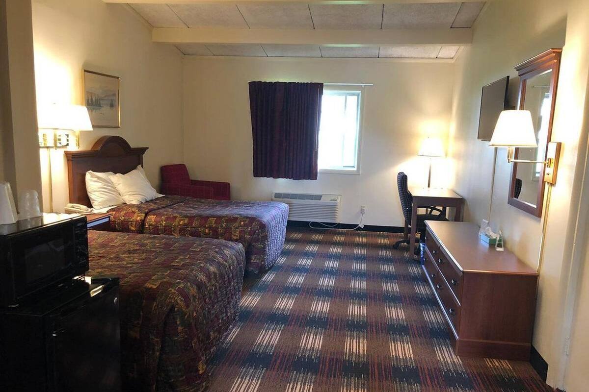A hotel room with two beds, a desk, a chair, a television, and a window with curtains.