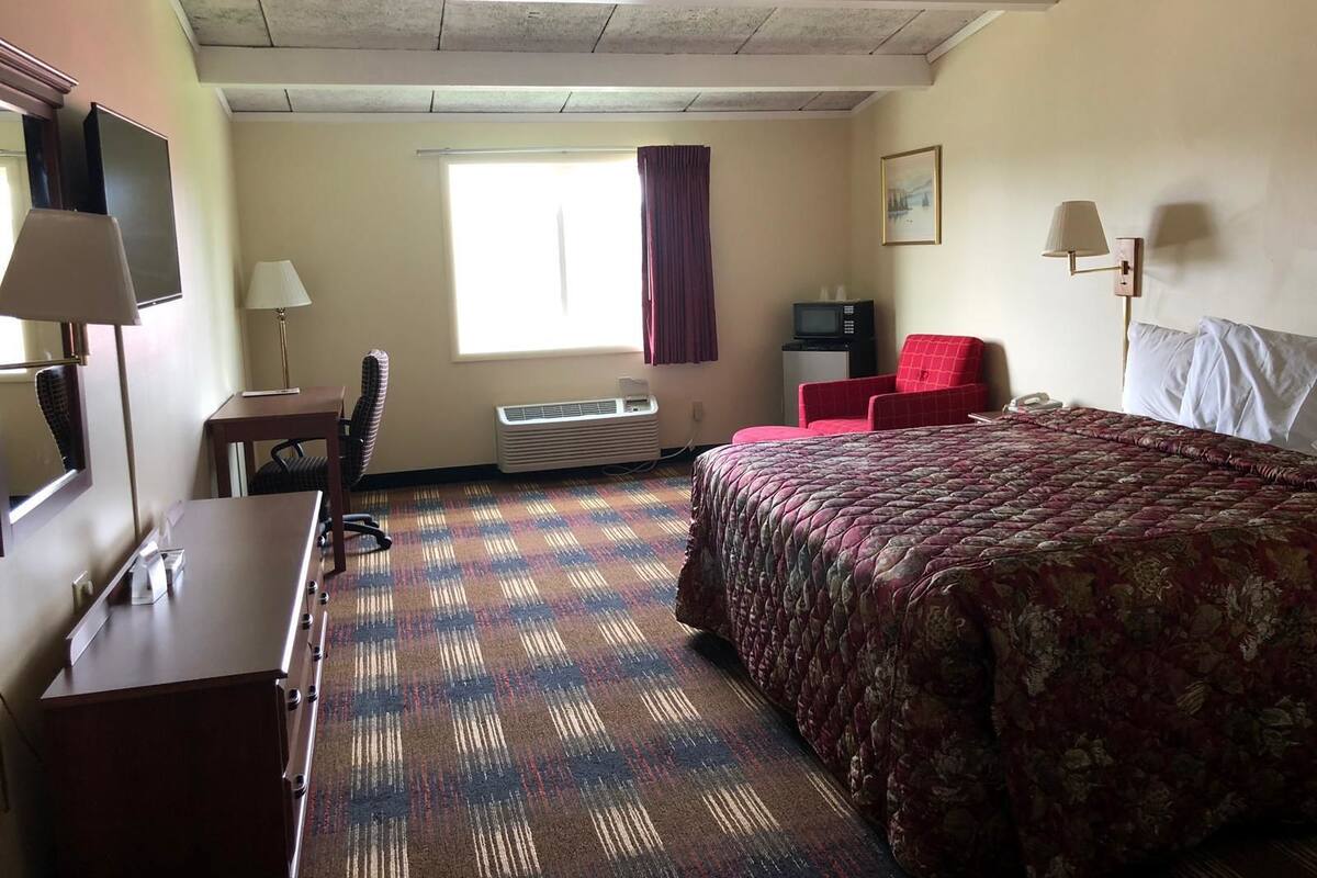 A hotel room with a bed, a desk, a chair, a television, and a window with curtains.