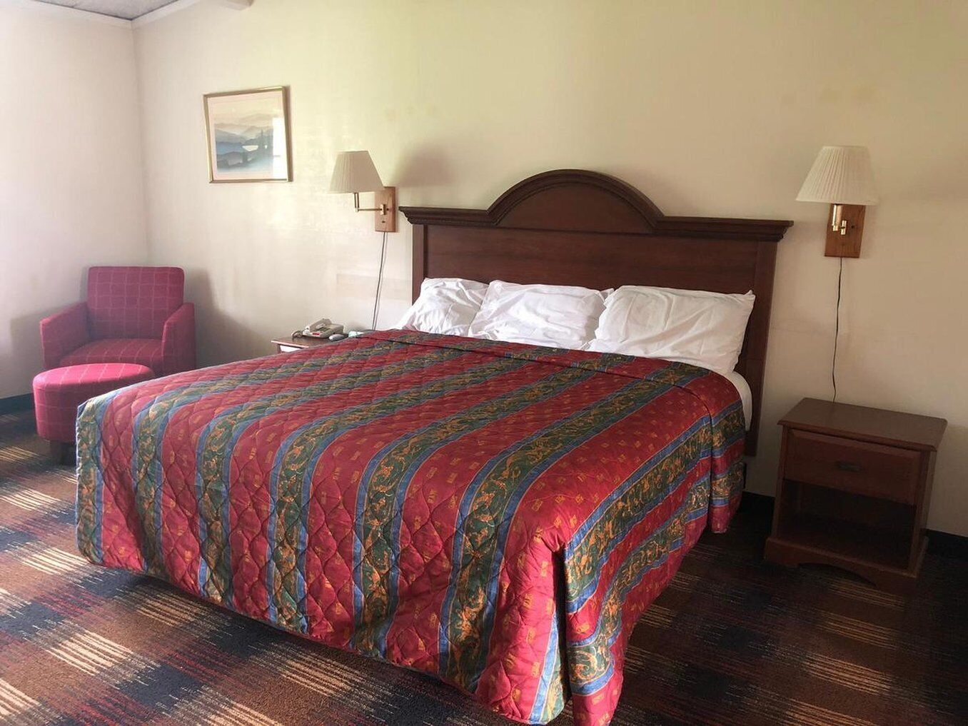 Une chambre d’hôtel avec un grand lit, une chaise, deux tables de chevet et un tableau au mur.