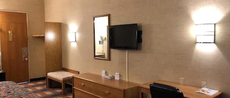A hotel room with a bed, a desk, a chair, a television, and a mirror.
