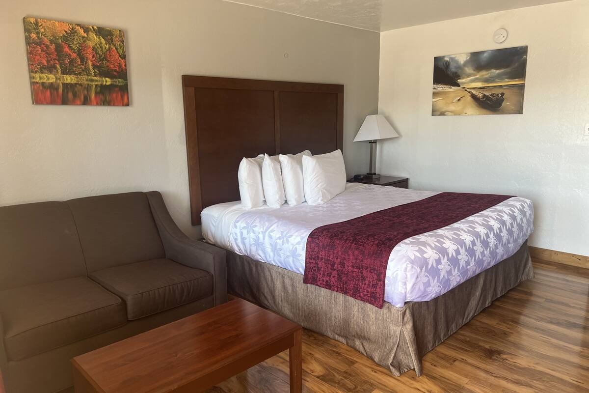 Une chambre d’hôtel avec un lit, une table de chevet en bois, une lampe, un canapé marron et une table basse en bois.