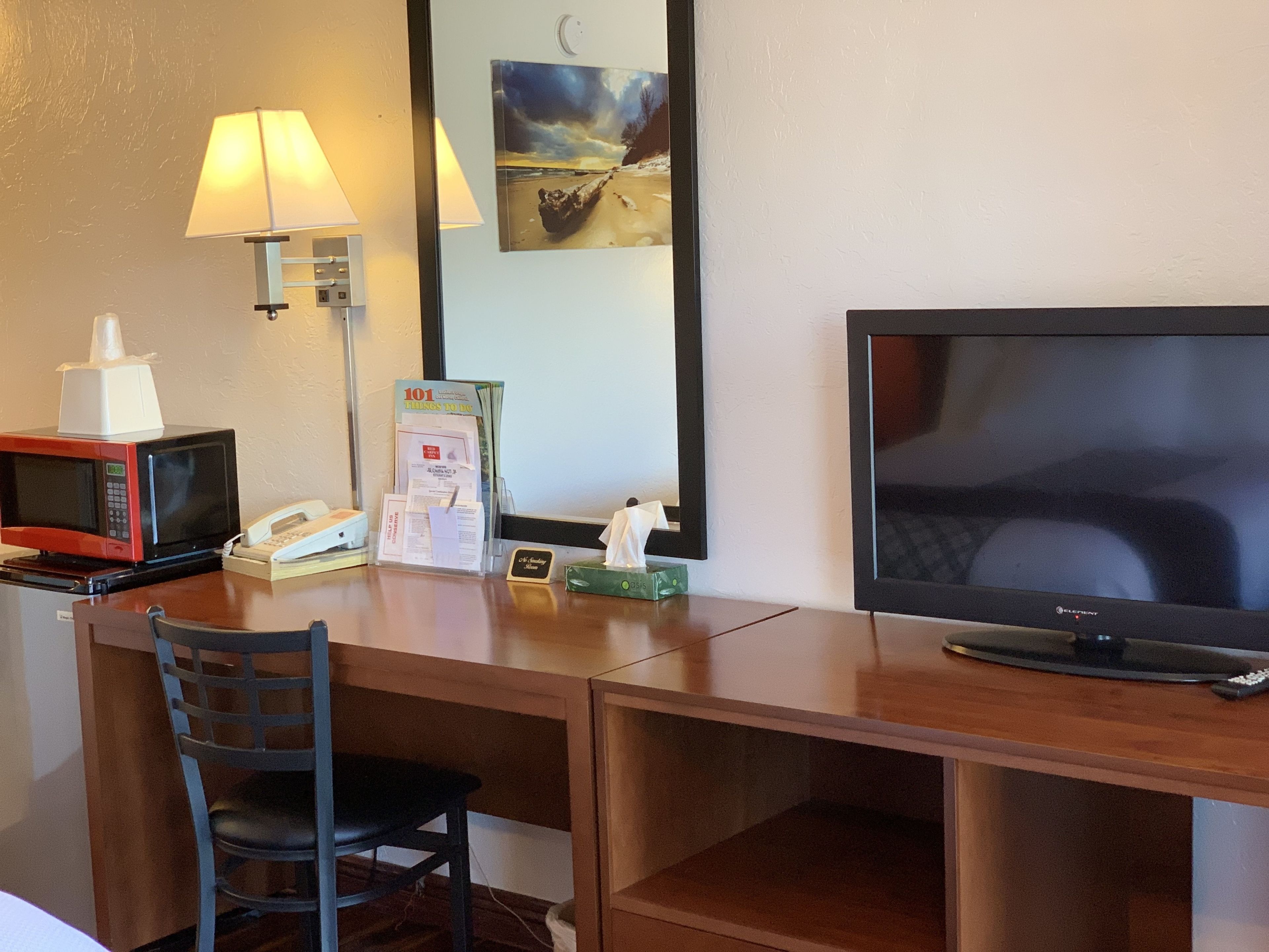 Escritorio de habitación de hotel con microondas, teléfono, lámpara y televisión.