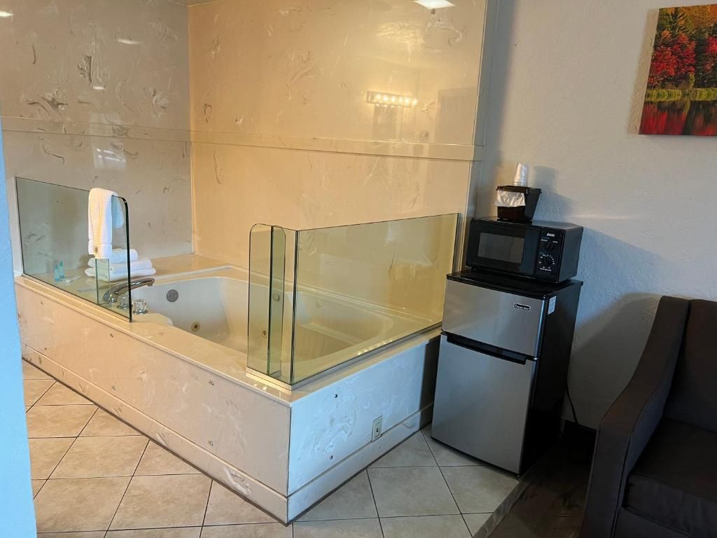 A bathroom with a glass-enclosed bathtub, a small refrigerator, and a microwave on a countertop.