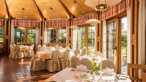 A dining area with wooden ceiling beams, large windows, and tables set for a meal.