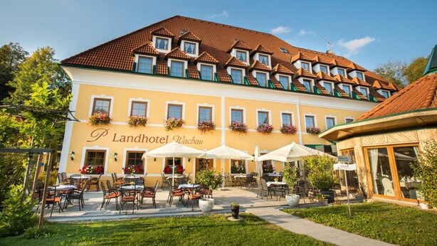 A hotel with a yellow facade, multiple windows, outdoor seating, and a sign reading "Landhotel Wachau".