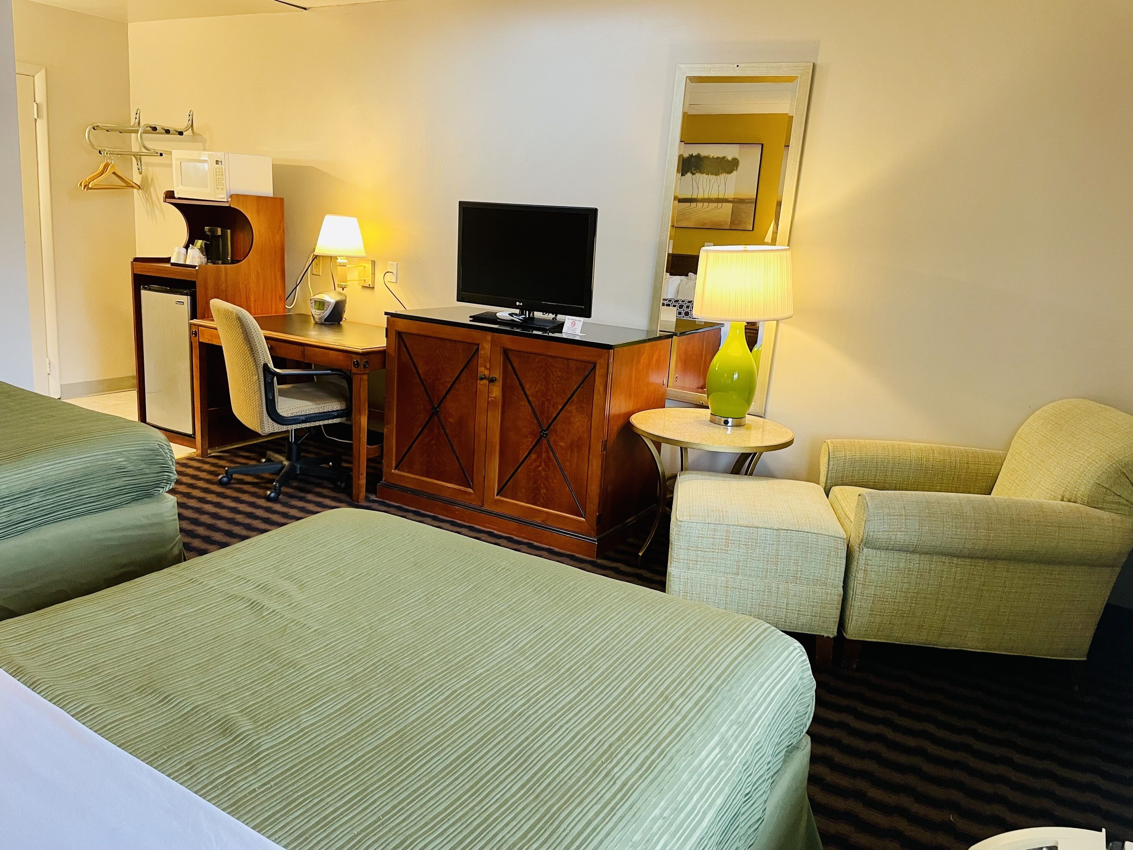 Una habitación de hotel con dos camas individuales, un escritorio con ordenador y lámpara, un televisor y una mesita con lámpara.