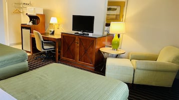 A hotel room with two single beds, a desk with a computer and lamp, a television, and a small table with a lamp.