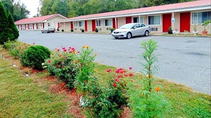 A motel with a row of single-story buildings, each with a red roof and white walls. There are several cars parked in front, and a variety of plants and flowers in the foreground. - Red Carpet Inn Duncannon (Duncannon)
