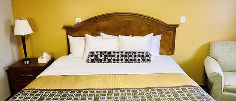 Una habitación de hotel con una cama, una mesita de noche con lámpara y una silla.