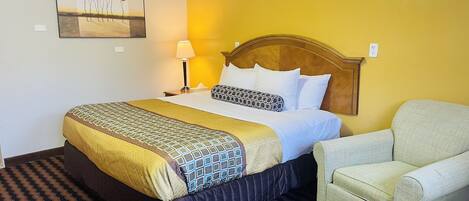 Una habitación de hotel con cama, una silla, una lámpara y un cuadro en la pared.