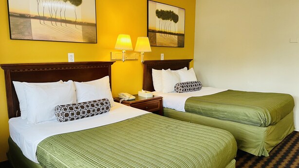 A hotel room with two beds, each with green bedding and white pillows. There are two wall-mounted lamps on the nightstands. - Red Carpet Inn Duncannon (Duncannon)