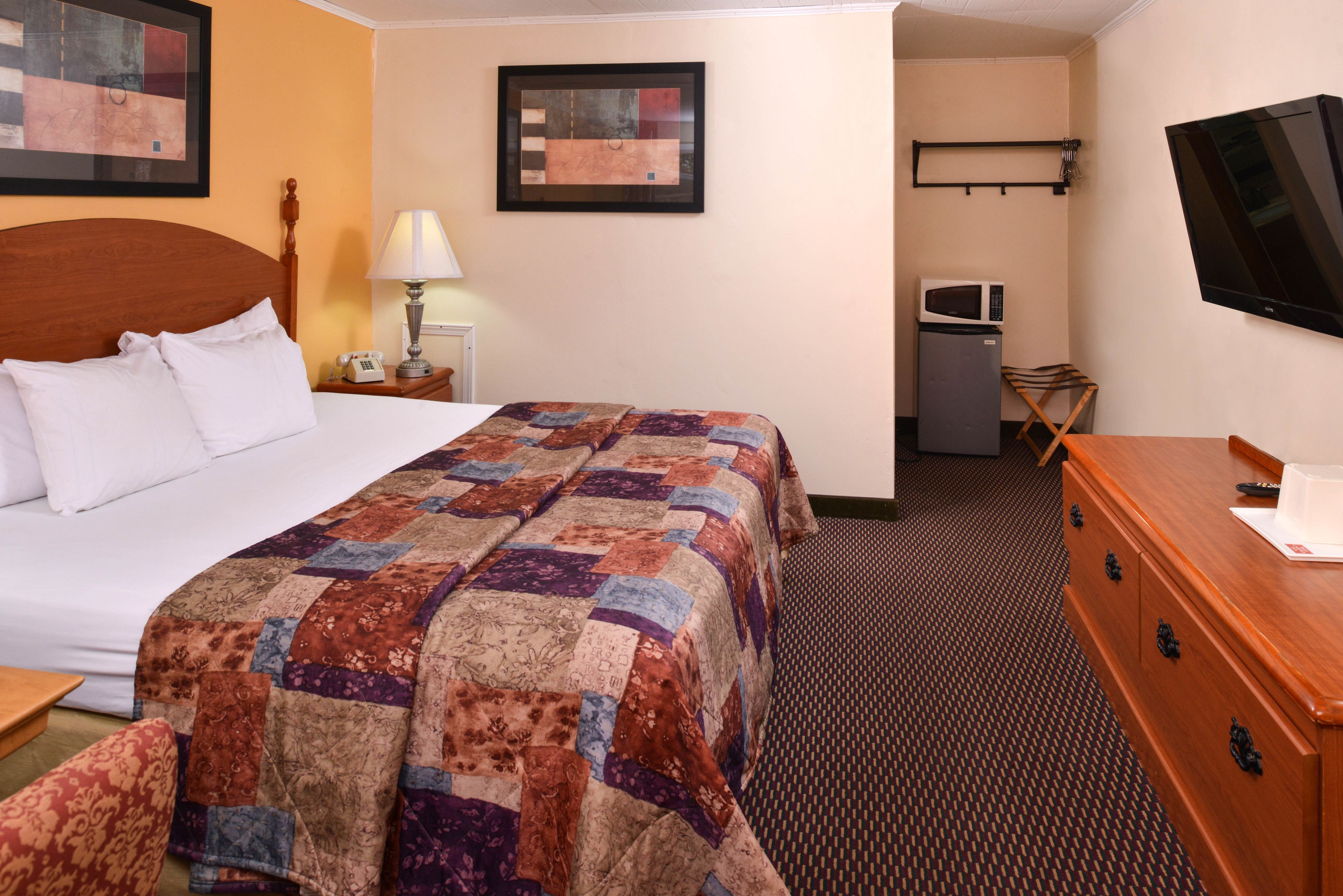 A hotel room with a bed, a desk, a dresser, a TV, a microwave, and a small seating area.