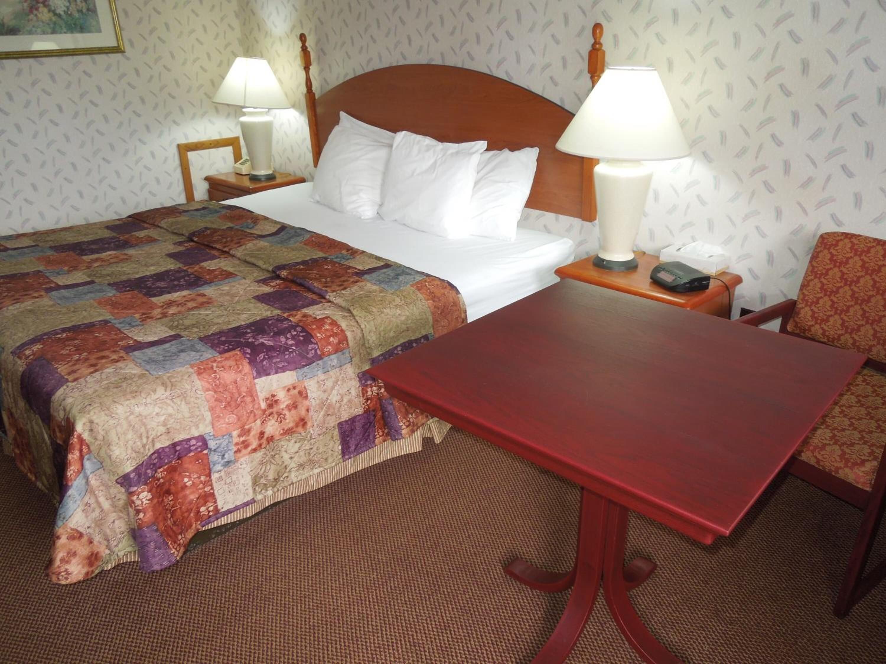 A hotel room with a bed, two bedside lamps, a red table, and a patterned carpet.