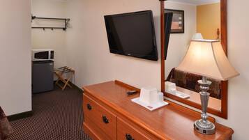 Habitación de hotel con tocador de madera, televisor de pantalla plana montado en la pared, lámpara, microondas y una mesita con un control remoto.