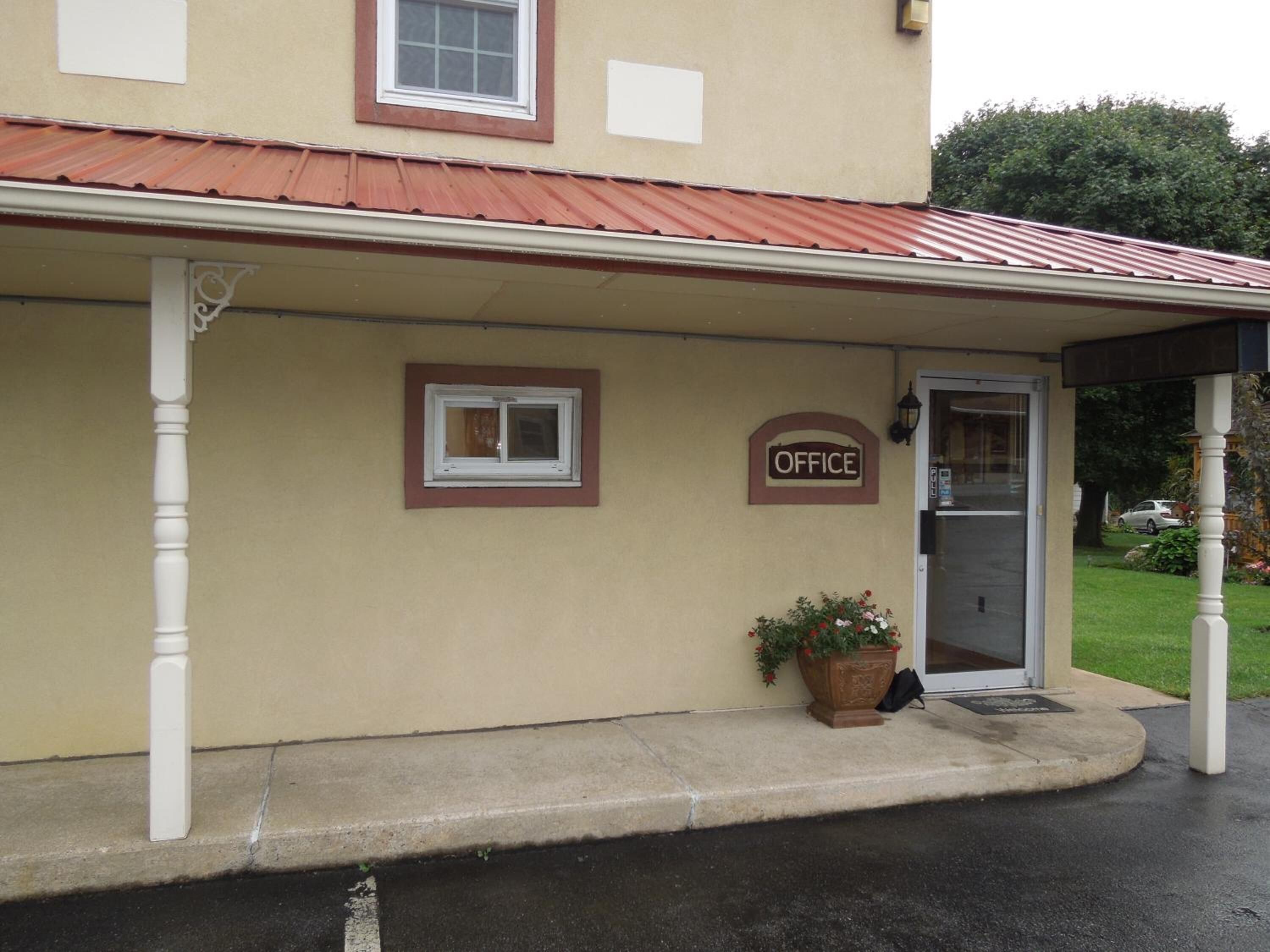 A building with a beige exterior, a red roof, and a sign that reads "OFFICE". There is a potted plant on the ground.