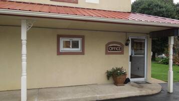 A building with a beige exterior, a red roof, and a sign that reads "OFFICE". There is a potted plant on the ground.