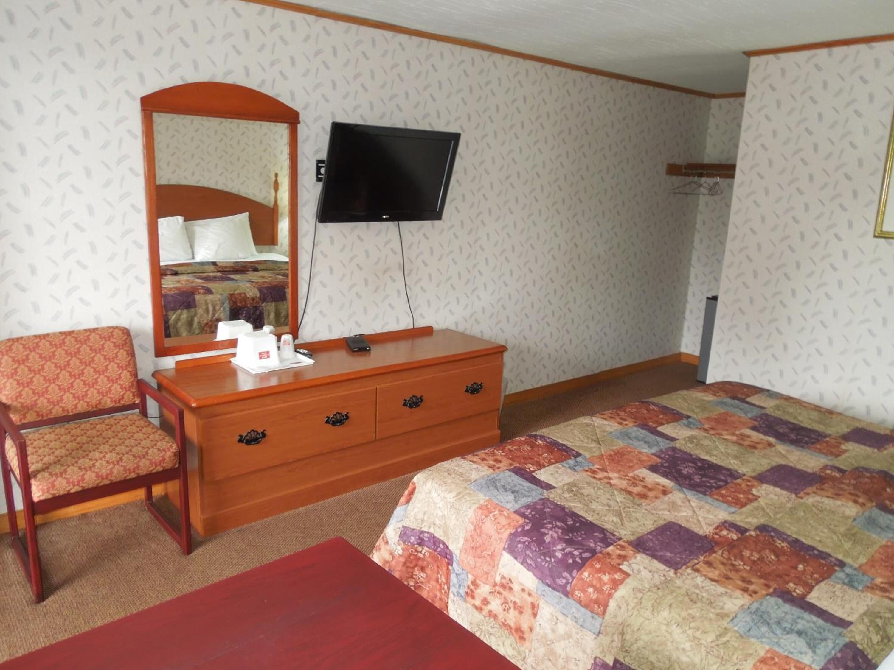 A hotel room with a bed, a wooden dresser, a chair, a television, and a mirror.