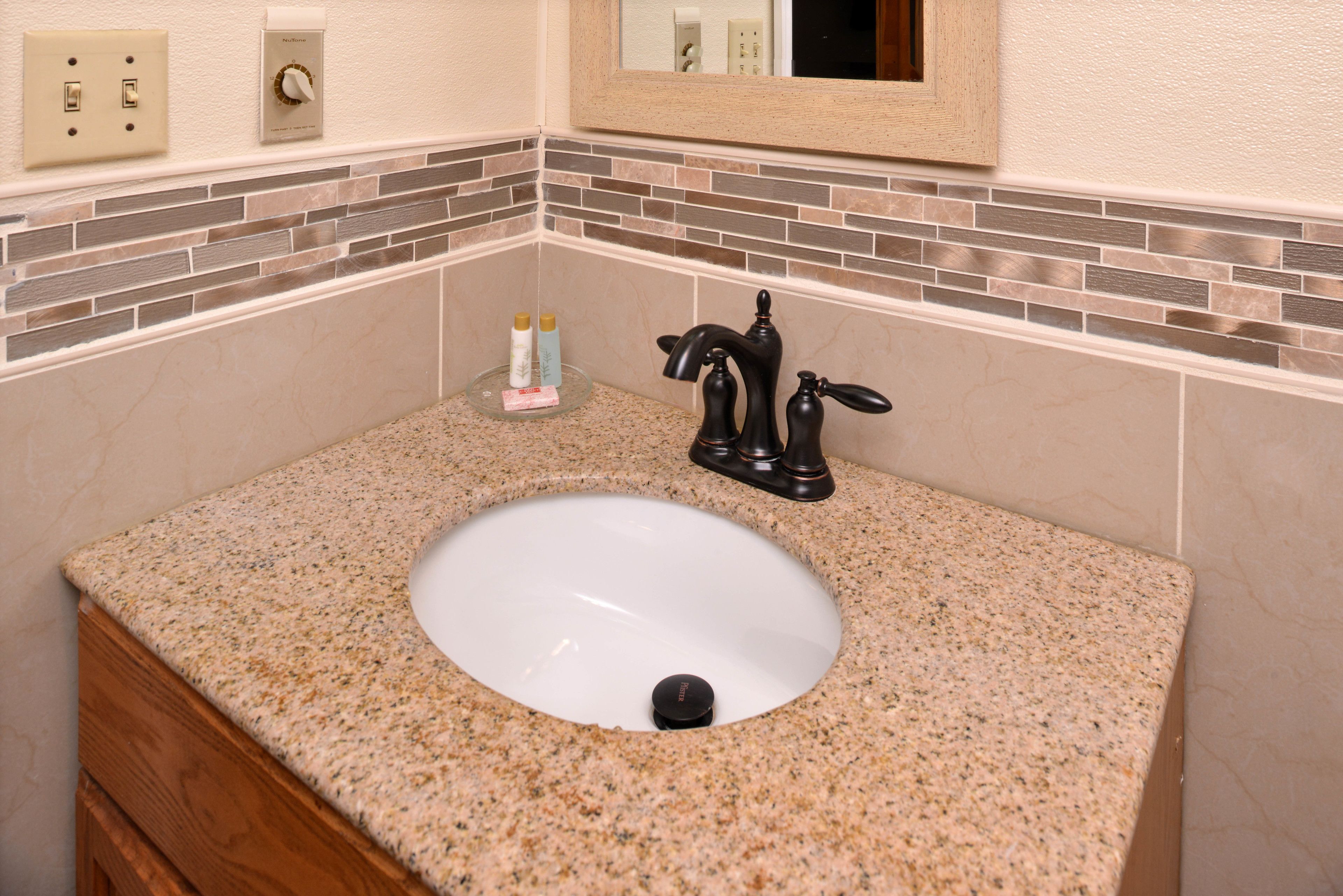 A bathroom with a granite countertop, a white sink, a black faucet, and a mirror above the sink.