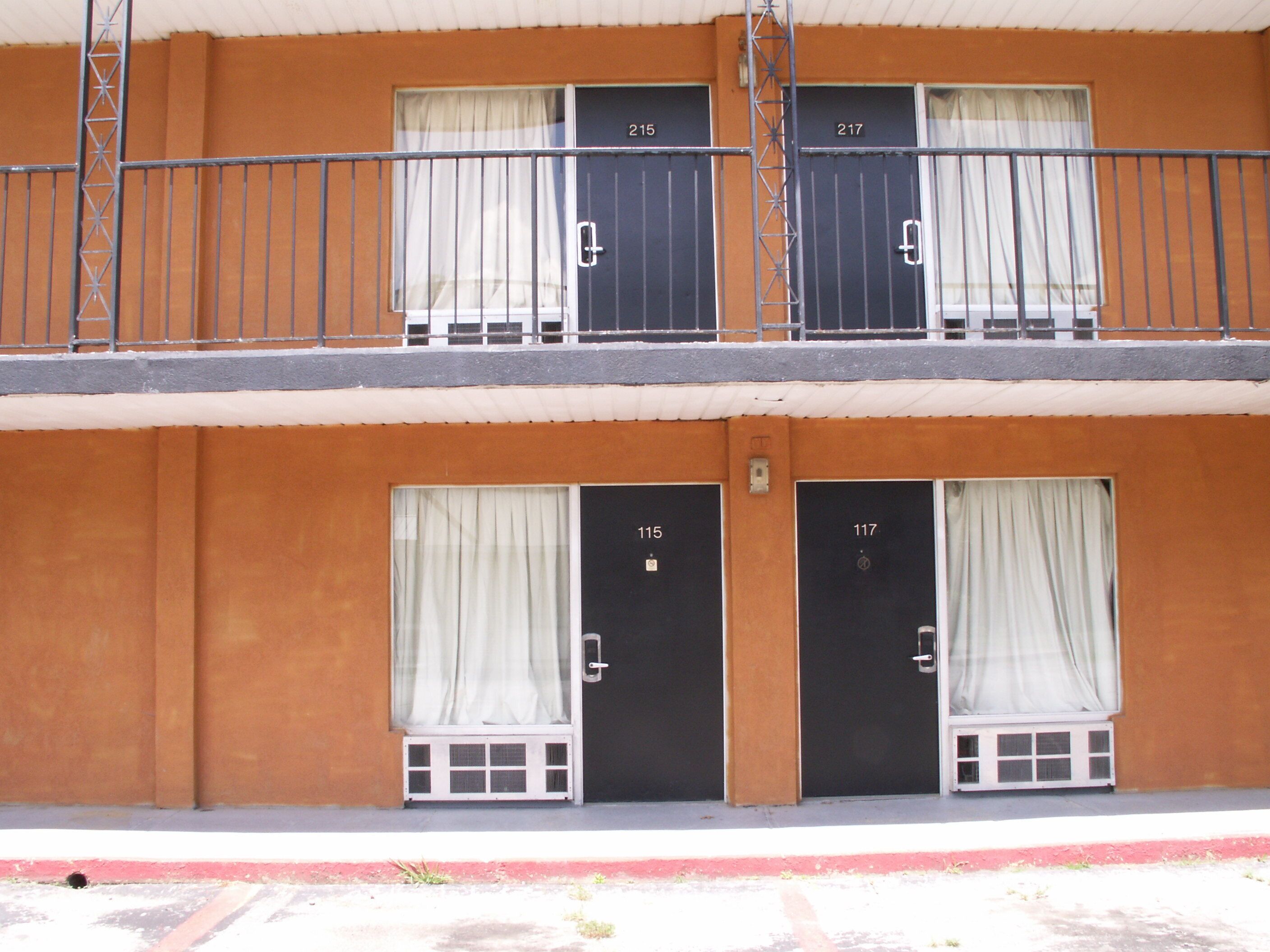 A two-story building with numbered doors (115, 117, 215, 217) and a balcony with a metal railing.
