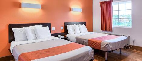 A hotel room with two beds, wooden flooring, a window with curtains, and wall-mounted lighting.