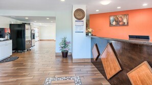 Eine Hotlellobby mit einer Rezeption, einer Uhr und einer Wandtafel mit Speisekarte.