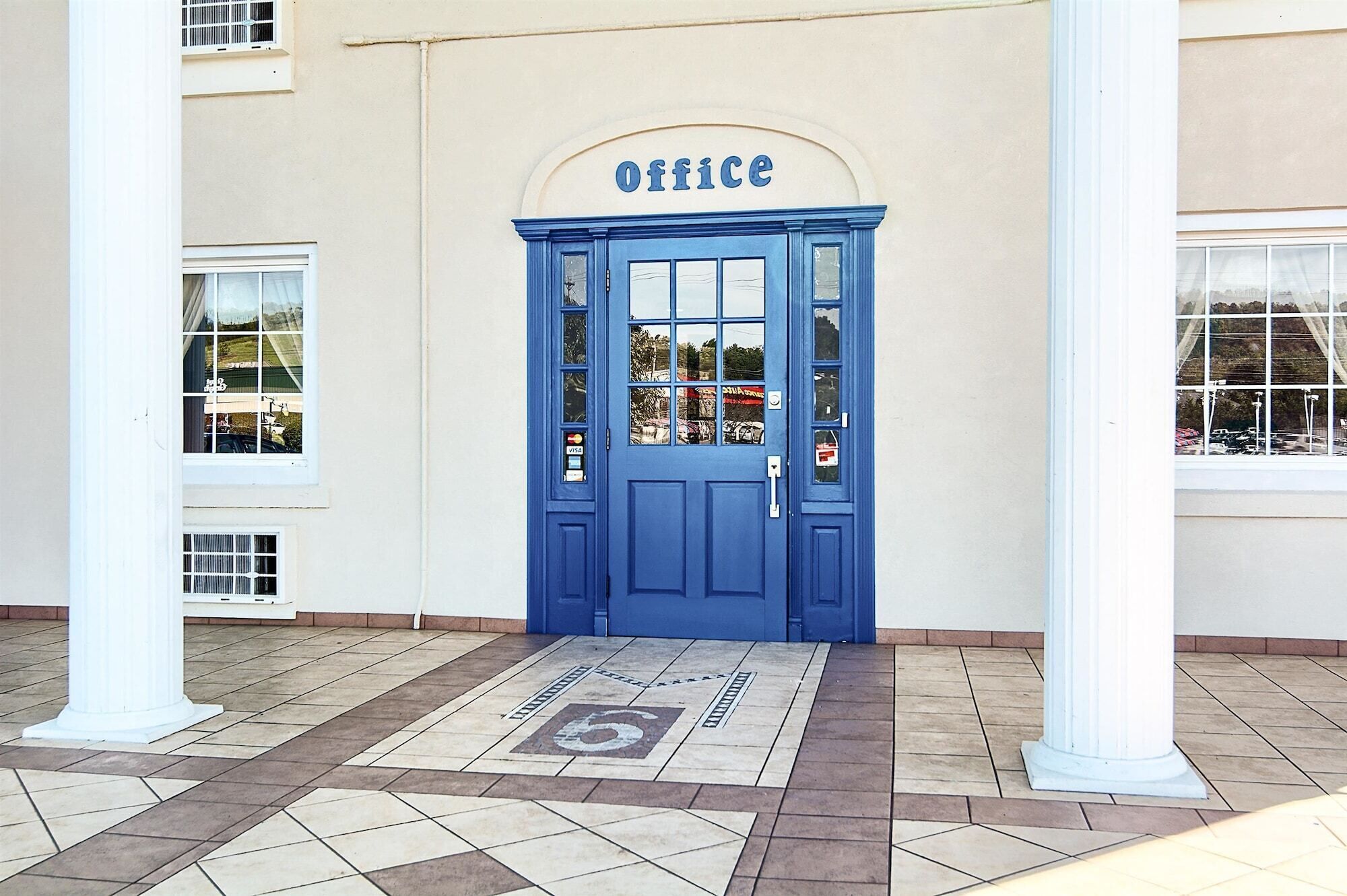 A blue door with a sign reading "office" above it, leading to a building with white columns and a tiled entrance area.