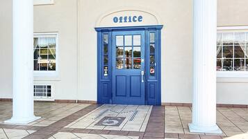 A blue door with a sign reading "office" above it, leading to a building with white columns and a tiled entrance area.