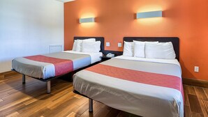 Ein Hotelzimmer mit zwei Betten, Holzboden und orangefarbenen Wänden.