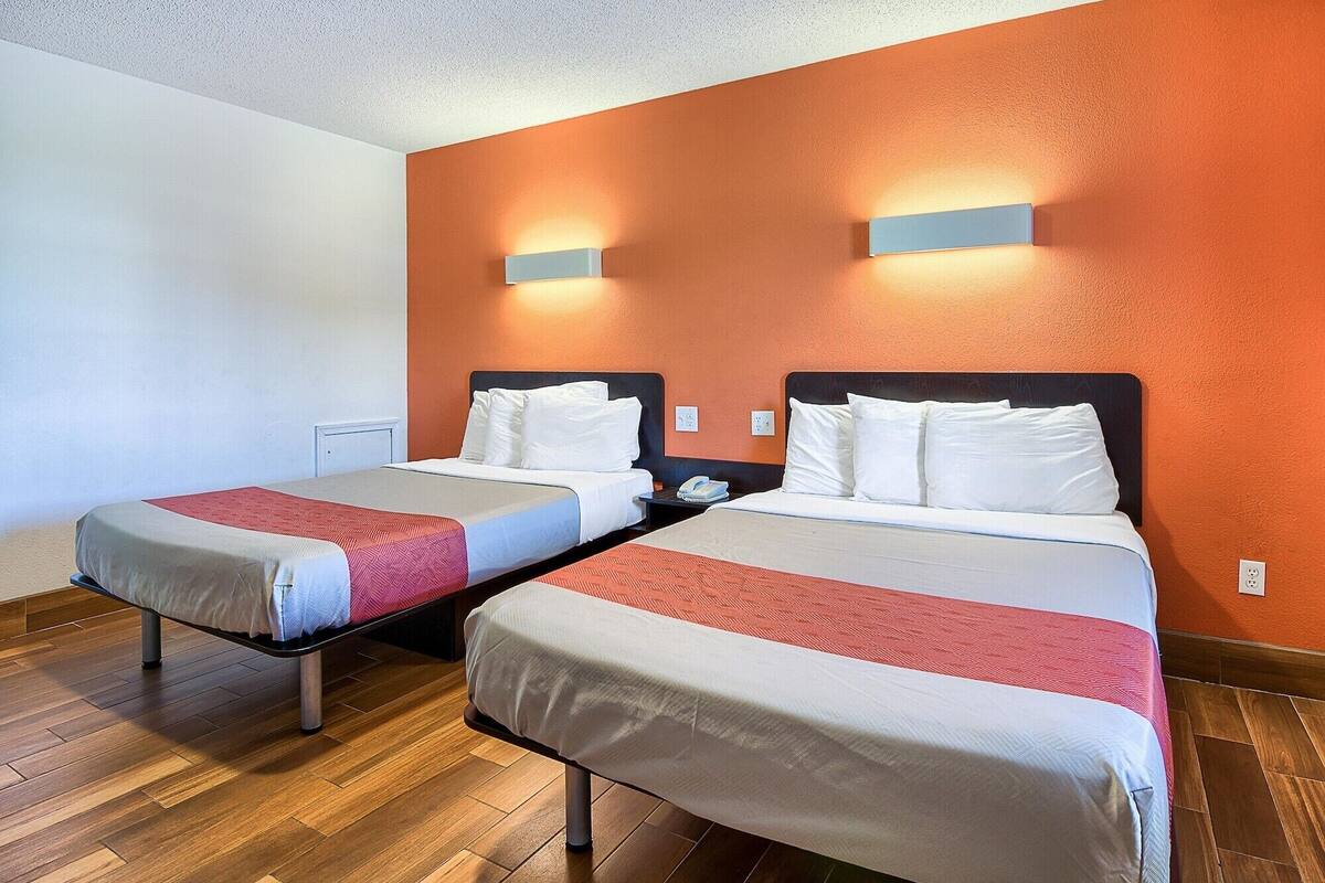 A hotel room with two beds, wooden flooring, and orange walls.