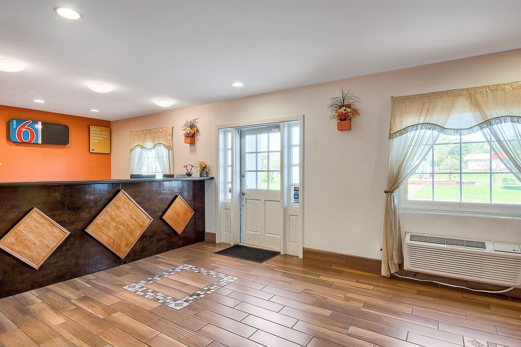 A reception area with a wooden floor, a reception desk, a door, and a window with a view of the outside.