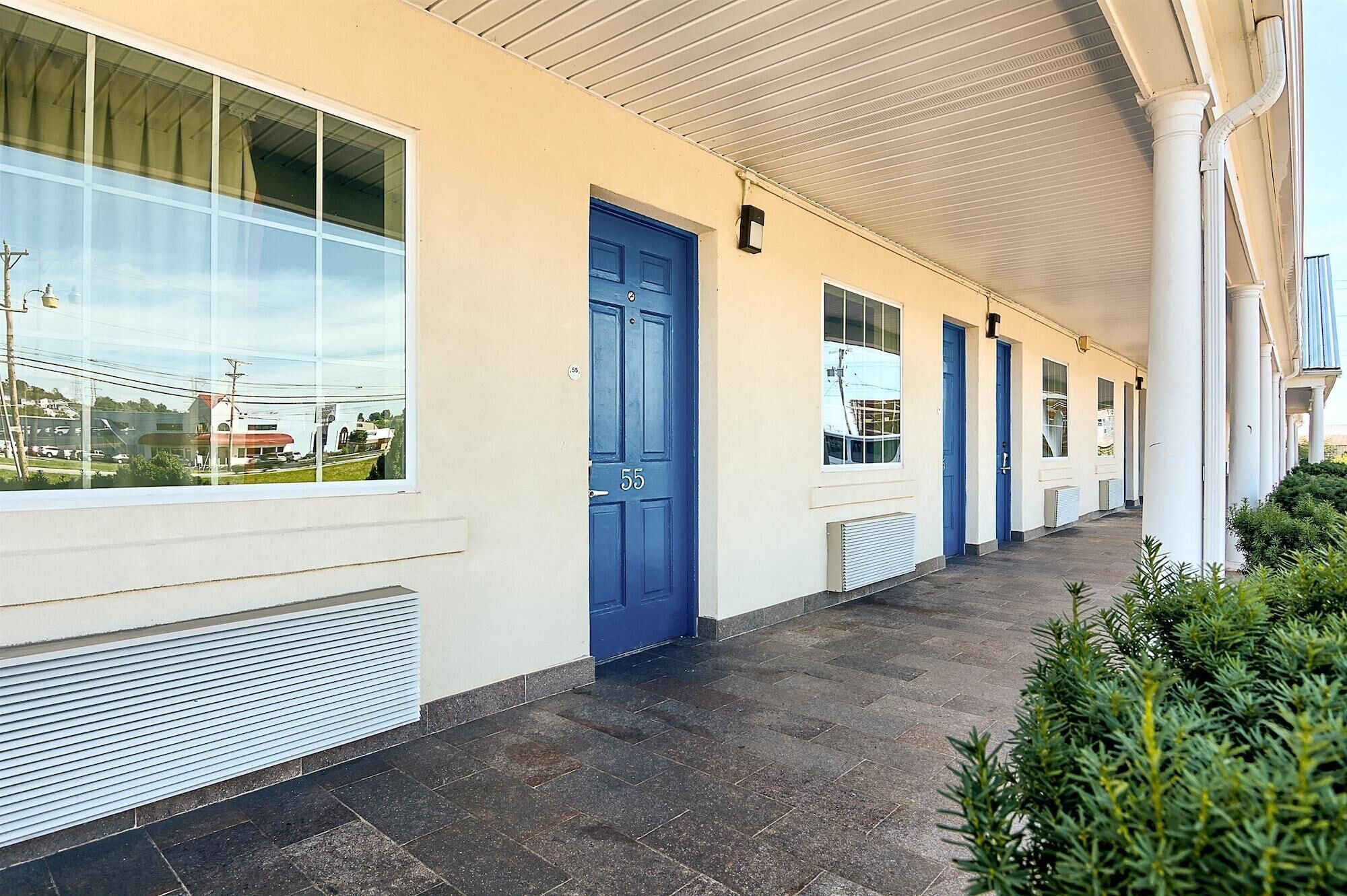 A hotel corridor with blue doors, large windows, and a covered walkway.