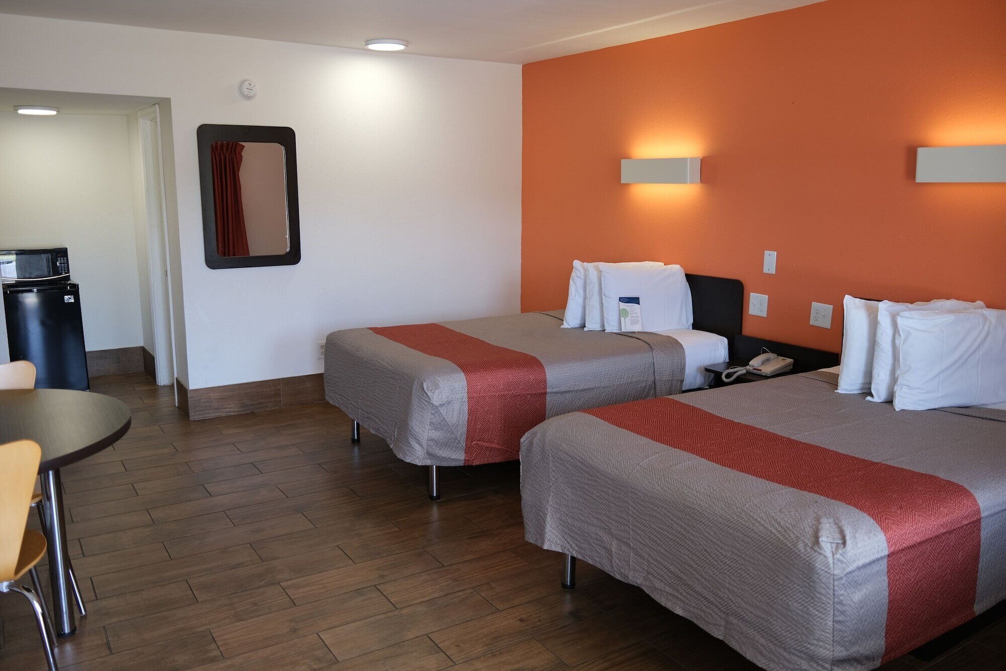 Habitación de hotel con dos camas, un escritorio, un microondas y un reloj en la pared.