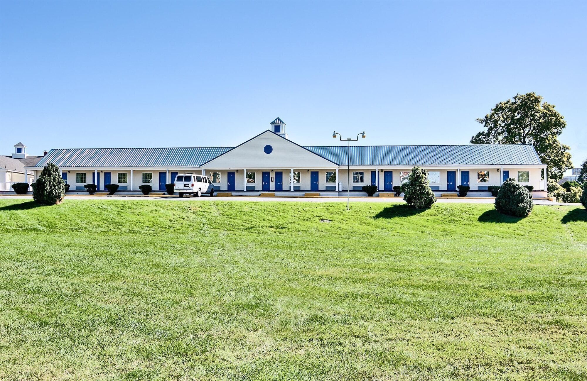 A motel with a row of rooms, a covered parking area, and a grassy lawn.