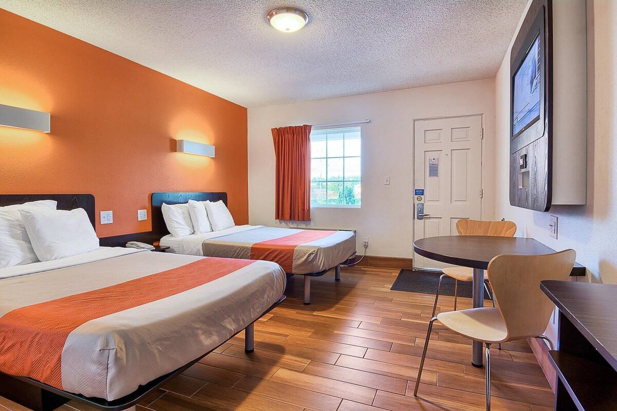 A hotel room with two beds, a dining table, and a TV.