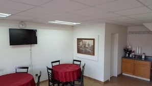 A room with a dining table, chairs, a flat-screen TV, a clock, a framed picture, and a kitchenette with cabinets and appliances. - Red Carpet Inn Blacksburg (Blacksburg)