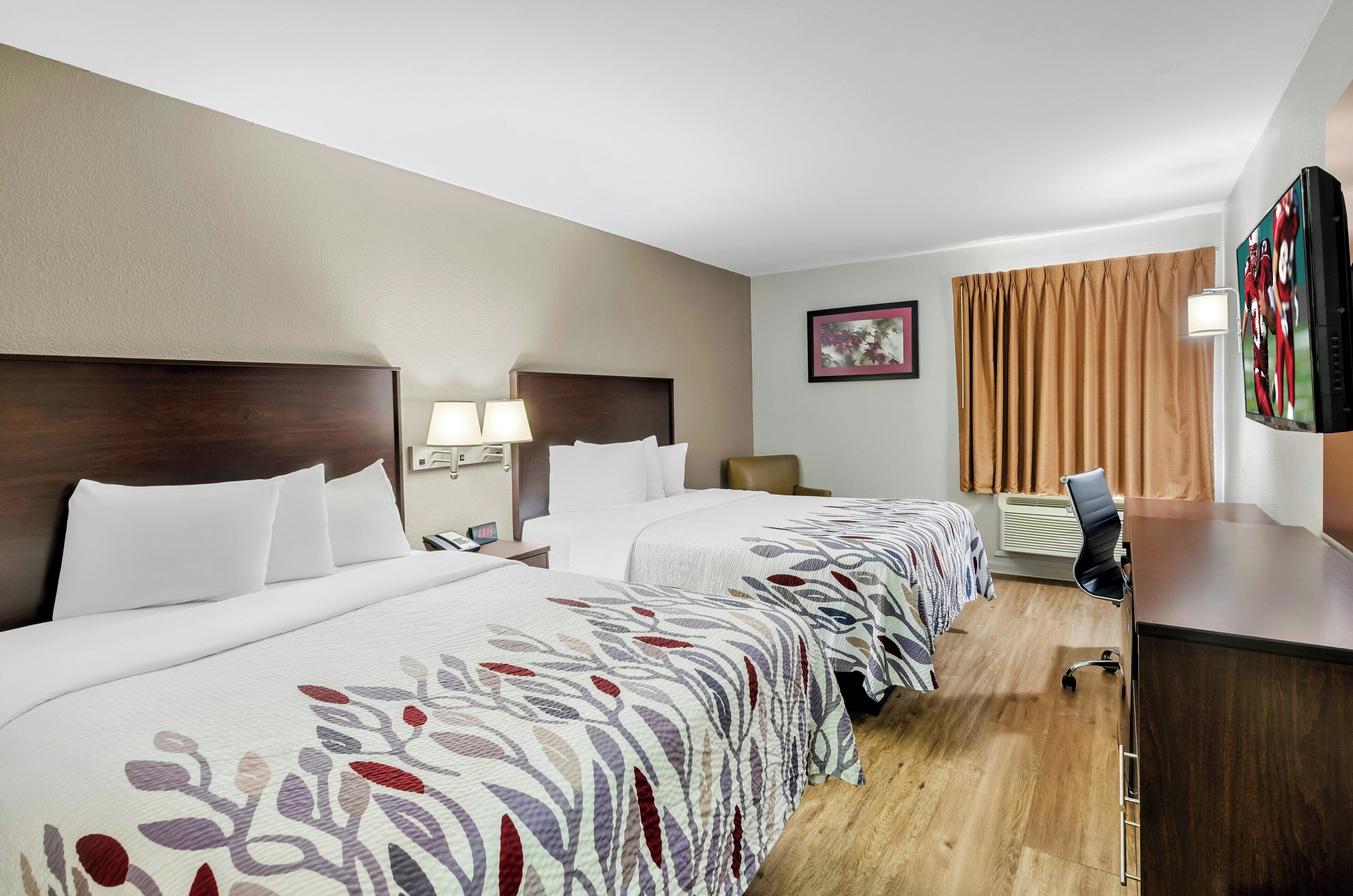 A hotel room with two beds, a desk, a chair, a TV, and a window with curtains.