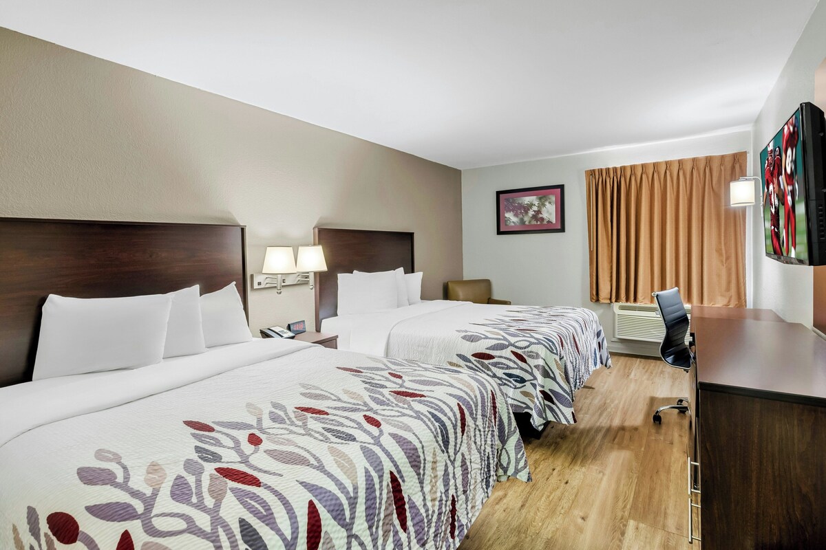 Hotelkamer met twee bedden, een bureau, een stoel, een televisie en een raam met gordijnen.