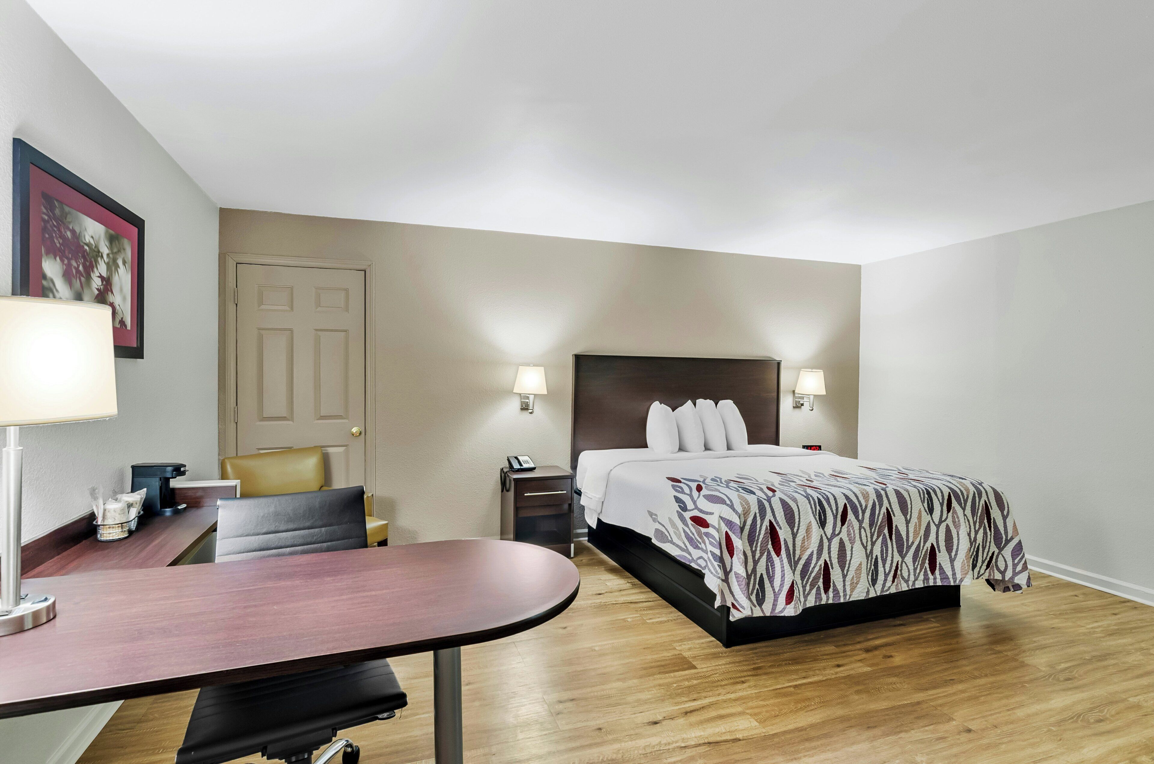 A hotel room with a bed, bedside tables, a desk, a chair, and a door.