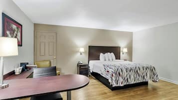 A hotel room with a bed, bedside tables, a desk, a chair, and a door.
