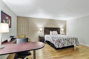 Une chambre d’hôtel avec un lit, des tables de chevet, un bureau, une chaise et une porte.