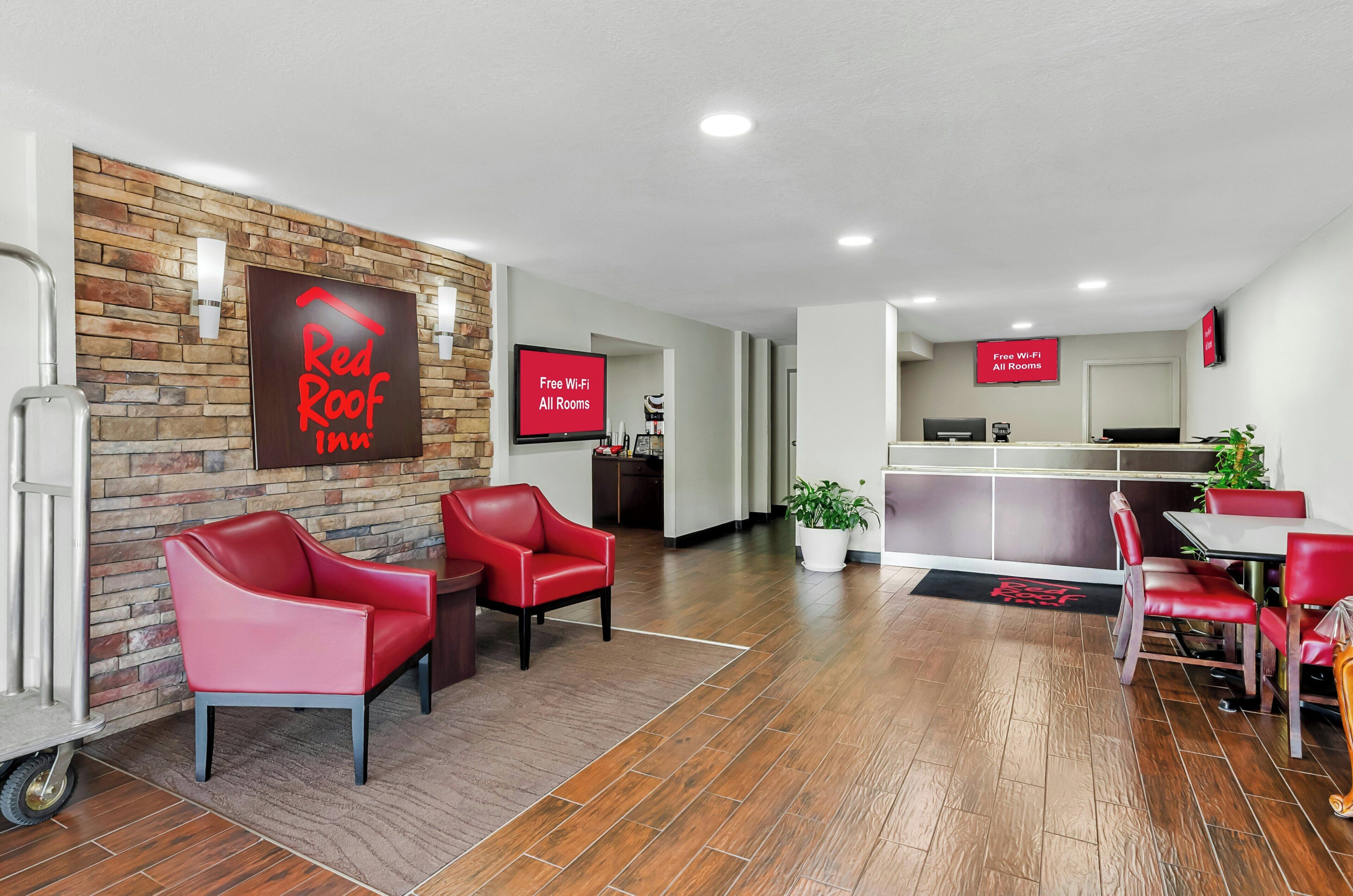 Vestíbulo de Red Roof Inn con pared de ladrillo, sillas rojas, mostrador de recepción y señal que indica Wi-Fi gratuito en todas las habitaciones.