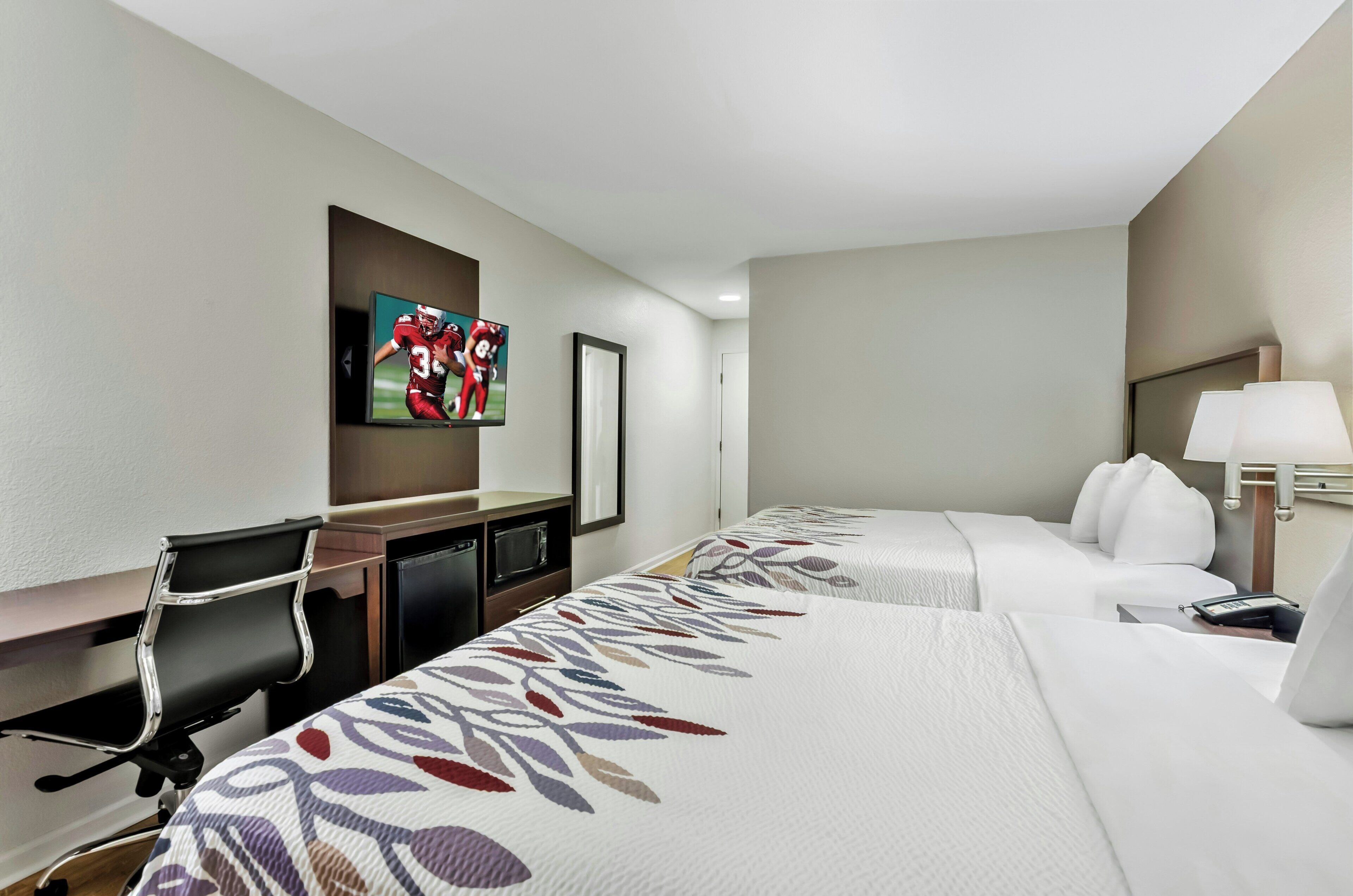 Camera d'albergo con due letti, una scrivania, una sedia, una televisione e una lampada.