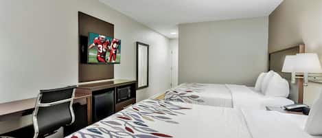 A hotel room with two beds, a desk, a chair, a TV, and a lamp.