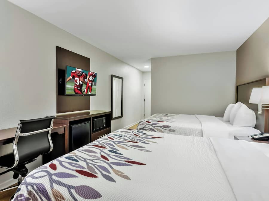 Une chambre d’hôtel avec deux lits, un bureau, une chaise, une télévision et une lampe.