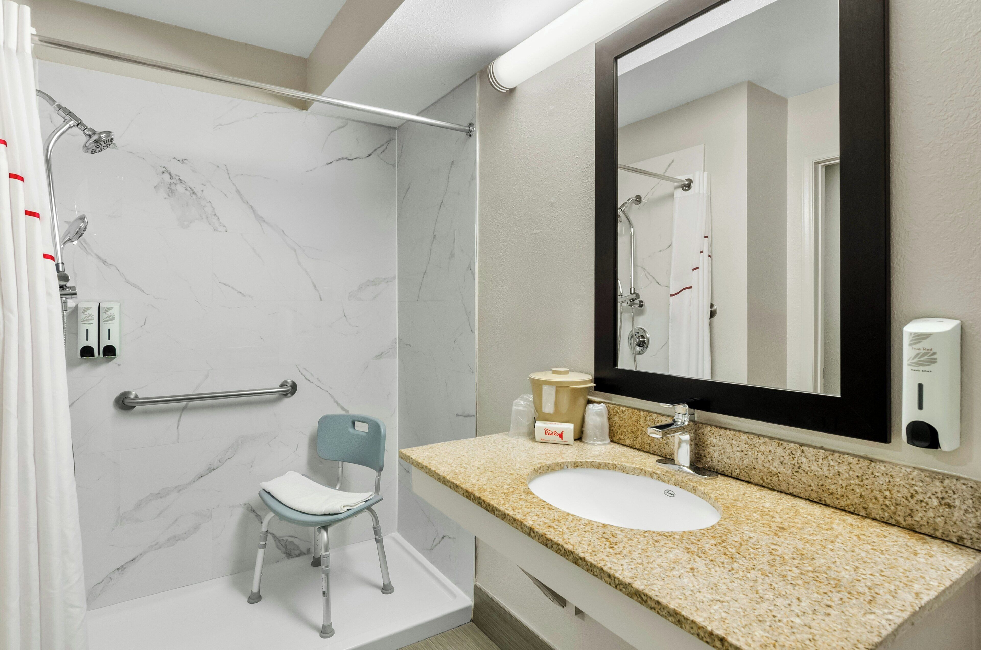 A modern bathroom with a shower, a sink, a chair, and a mirror.