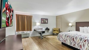 Une chambre d’hôtel avec un lit, un bureau, une chaise, une télévision et un tableau encadré au mur.