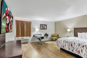 Hotelkamer met een bed, bureau, stoel, televisie en een ingelijste foto aan de muur.