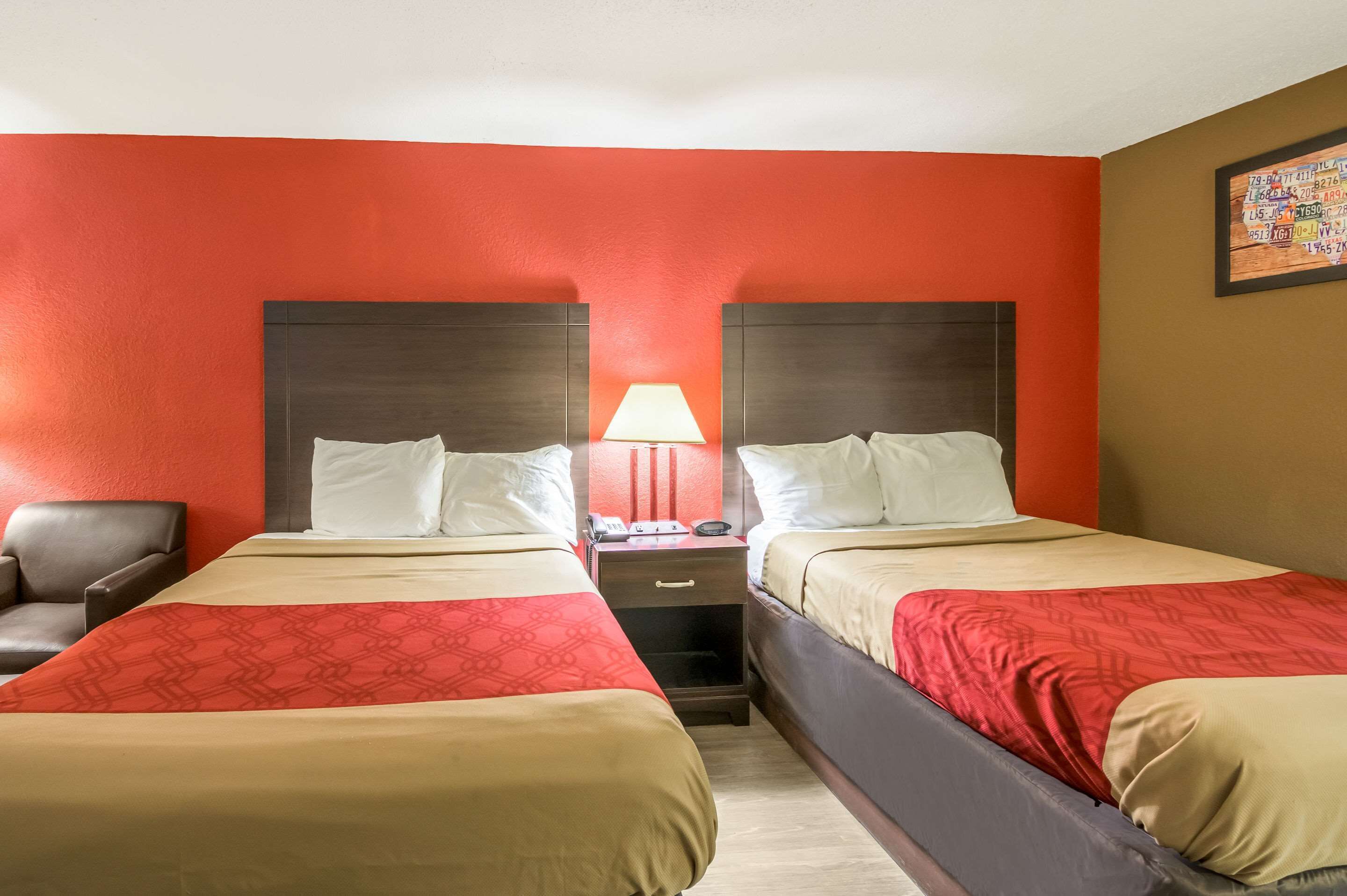 Una habitación de hotel con dos camas, una mesita de noche con una lámpara y una silla.